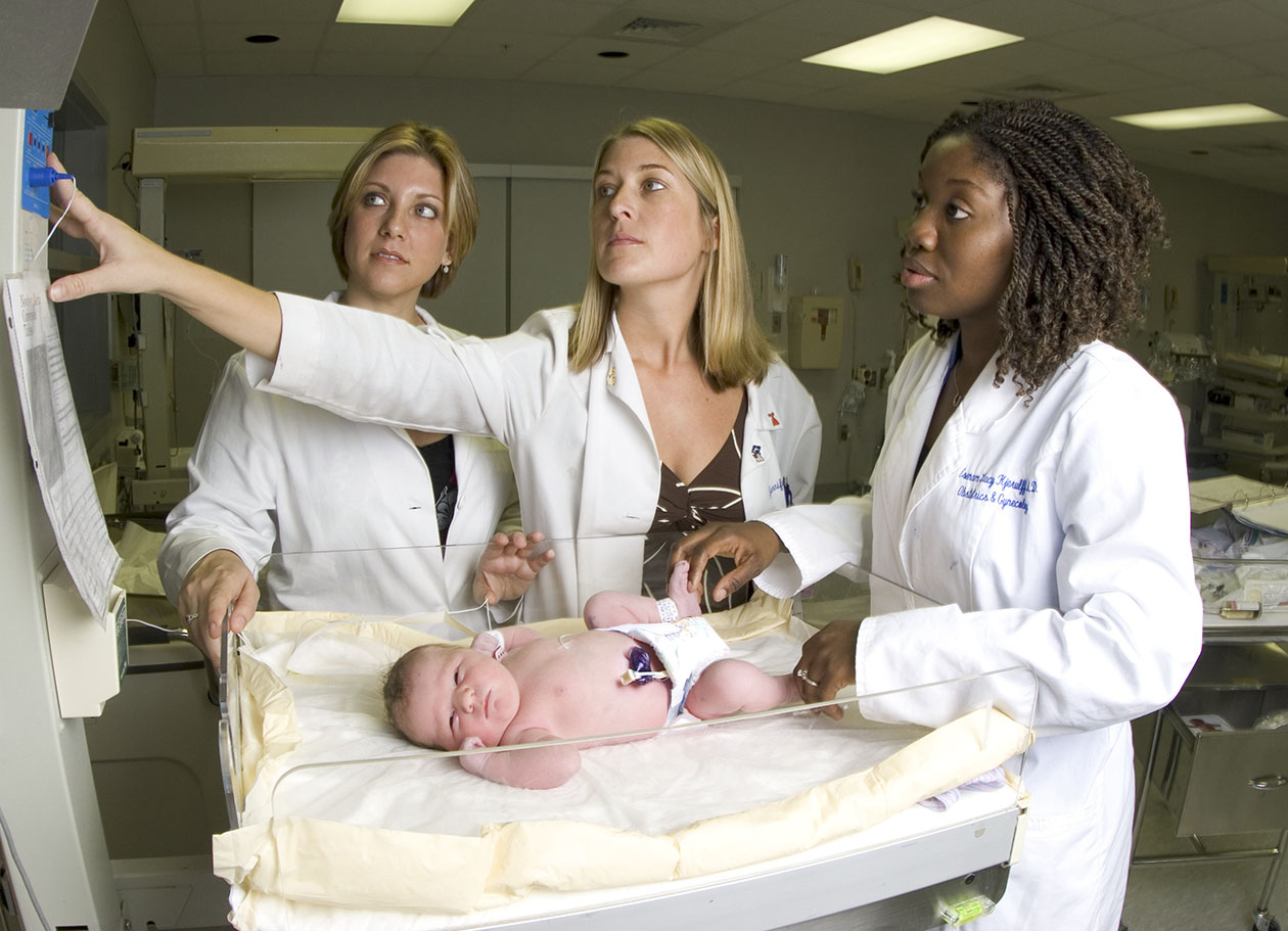 Three University of Florida obstetrics and gynecology resident physicians examine a newborn at the UF Health Jacksonville Newborn Nursery